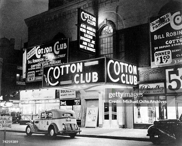 Exterior nighttime view of the marquee of the Cotton Club in New York, with cars in front.